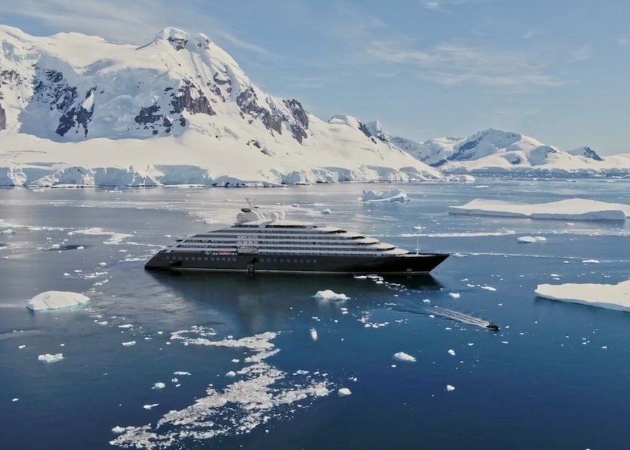 Scenic Eclipse cruise ship anchored in deep blue waters with snow-capped mountains and glaciers in the background.